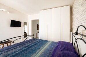 A bedroom with a bed, a TV, a wardrobe, and a brick wall.