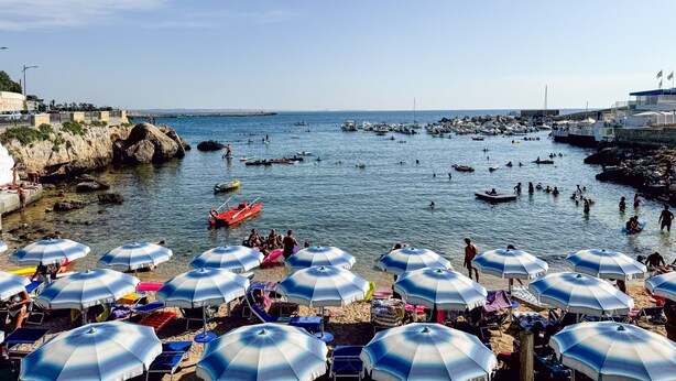 Une plage côtière bordée de nombreux parasols, de bateaux et de personnes.