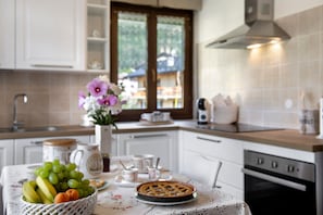 Una cocina con una mesa dispuesta para el té, incluyendo un pastel, fruta y tazas.