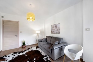 Una sala de estar moderna con un sofá gris, una silla blanca, un tapete de cuero de vaca, una lámpara colgante y un cuadro en la pared.