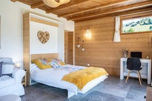 A bedroom with a bed, a desk, and a view of the outdoors.