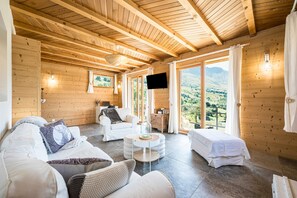 Un intérieur en bois comprenant un canapé, un pouf et un lit donnant sur l’extérieur.
