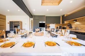 Un espace repas avec une longue table dressée pour le repas, des appareils de cuisine et un lambris en bois.