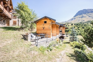 Une cabane en bois dotée d’un balcon, d’un mur en pierre et surplombant un paysage montagneux.