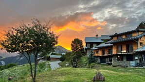 Ein rustikales Chalet mit Naturstein-Fassade, Holzbalkonen und Blick auf ein Gebirge.