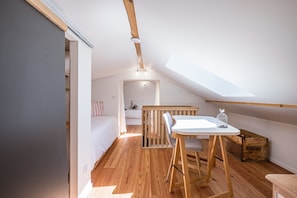 Une pièce de taille modeste avec un plafond en pente, une petite table avec des chaises, un banc en bois et, au fond, un berceau.
