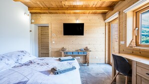 Ein Schlafzimmer mit Holzwandverkleidung, einem Bett, einem Schreibtisch und einem Fernseher.
