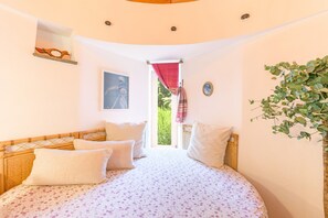 Une chambre à coucher avec un lit, des oreillers, une fenêtre donnant sur un beau paysage et une plante.