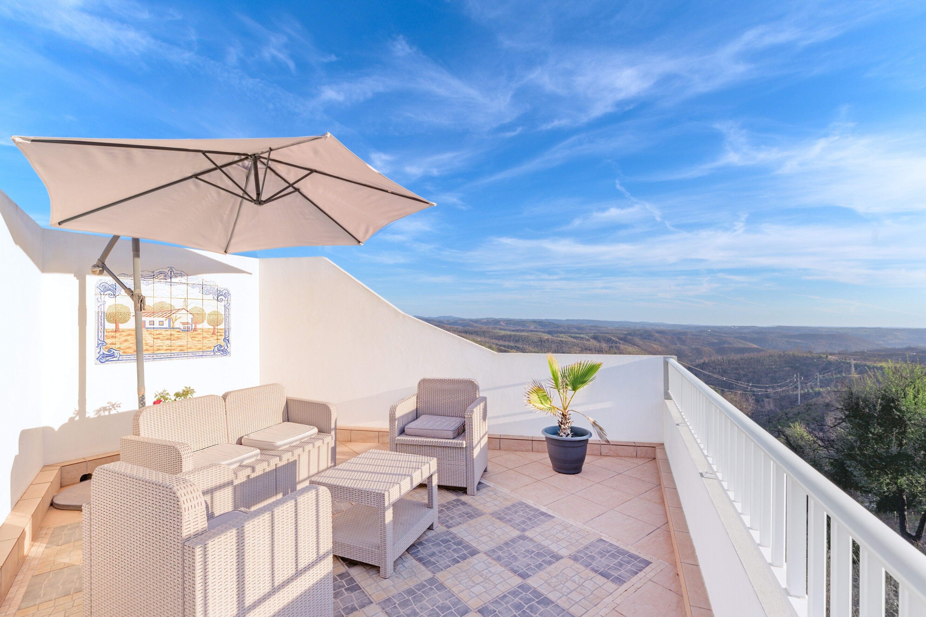 Un balcon agrémenté de meubles en osier, d’une plante en pot et offrant une vue sur le paysage.
