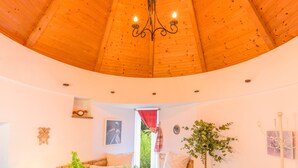 Une pièce avec un plafond en bois, un lustre, une plante et un tableau au mur.