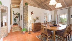 A dining area with a wooden table and chairs, a chandelier, and a view through the window. - Villa 'Sítio das Rolas - Selão da Eira' with Sea View, Private Pool and Wi-Fi (São Teotónio)