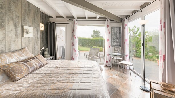 A bedroom with a large bed, a small table, and a chair near a sliding glass door leading to an outdoor area. - Villa 'Sítio das Rolas - Selão da Eira' with Sea View, Private Pool and Wi-Fi (São Teotónio)