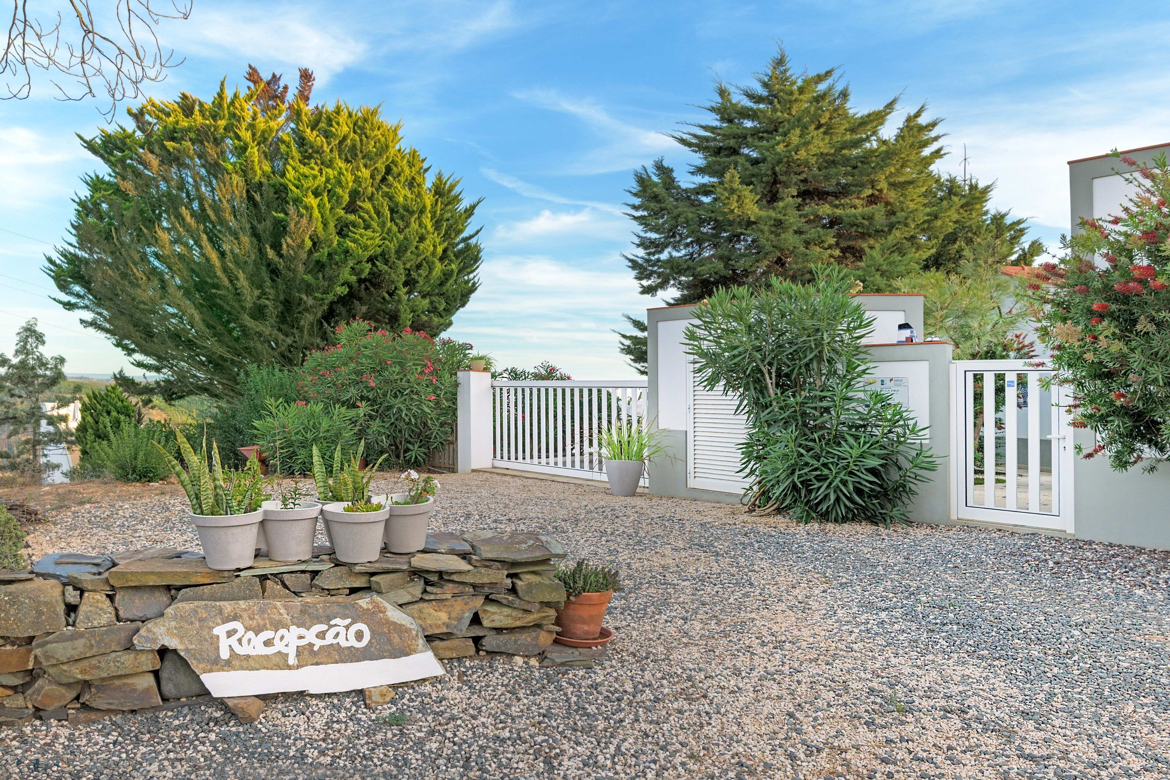 A gravel driveway leading to a gated entrance with potted plants and a stone wall.