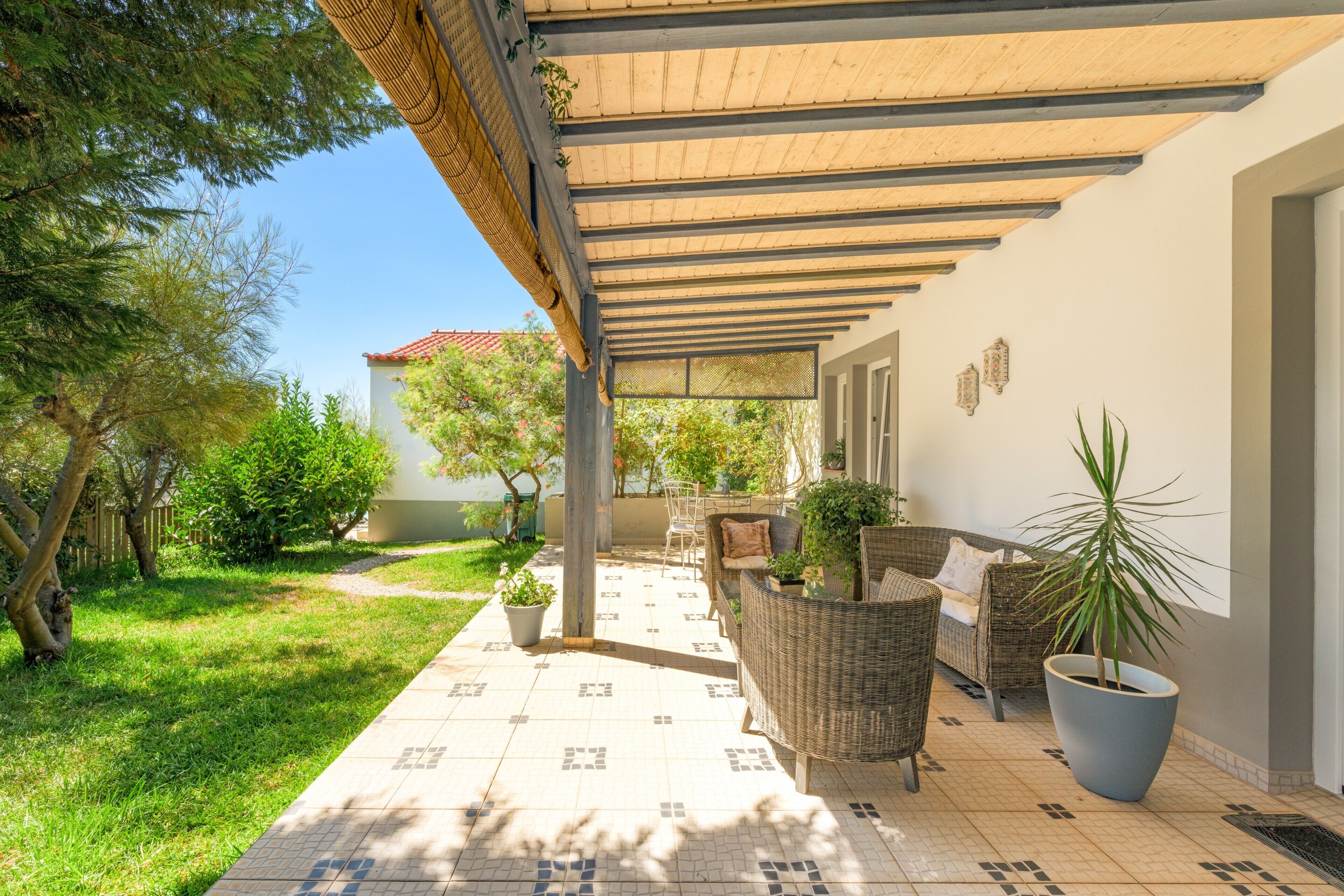 A covered outdoor patio with wicker furniture, potted plants, and a tiled floor.