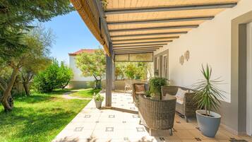 A covered outdoor patio with wicker furniture, potted plants, and a tiled floor.