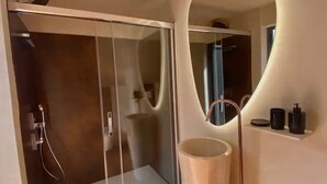 Ein modernes Badezimmer mit einer einteiligen Duschkabine, einem großen Spiegel und einem Waschbecken mit Pflegeprodukten.