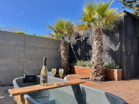 A patio with a wooden table, two chairs, a bottle of wine, and two glasses.