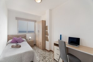 A bedroom with a bed, a desk with a laptop, a wardrobe, and a window with a view.