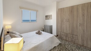 A bedroom with a bed, a wardrobe, a desk, a lamp, and a window with a view.