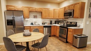 Une cuisine moderne avec des meubles en bois, des appareils en acier inoxydable et une table de salle à manger ronde, assortie de chaises.