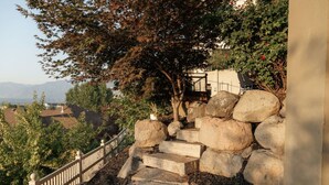 Un escalier en pierre mène à une terrasse en bois, qui est entourée de gros rochers et d’un arbre.