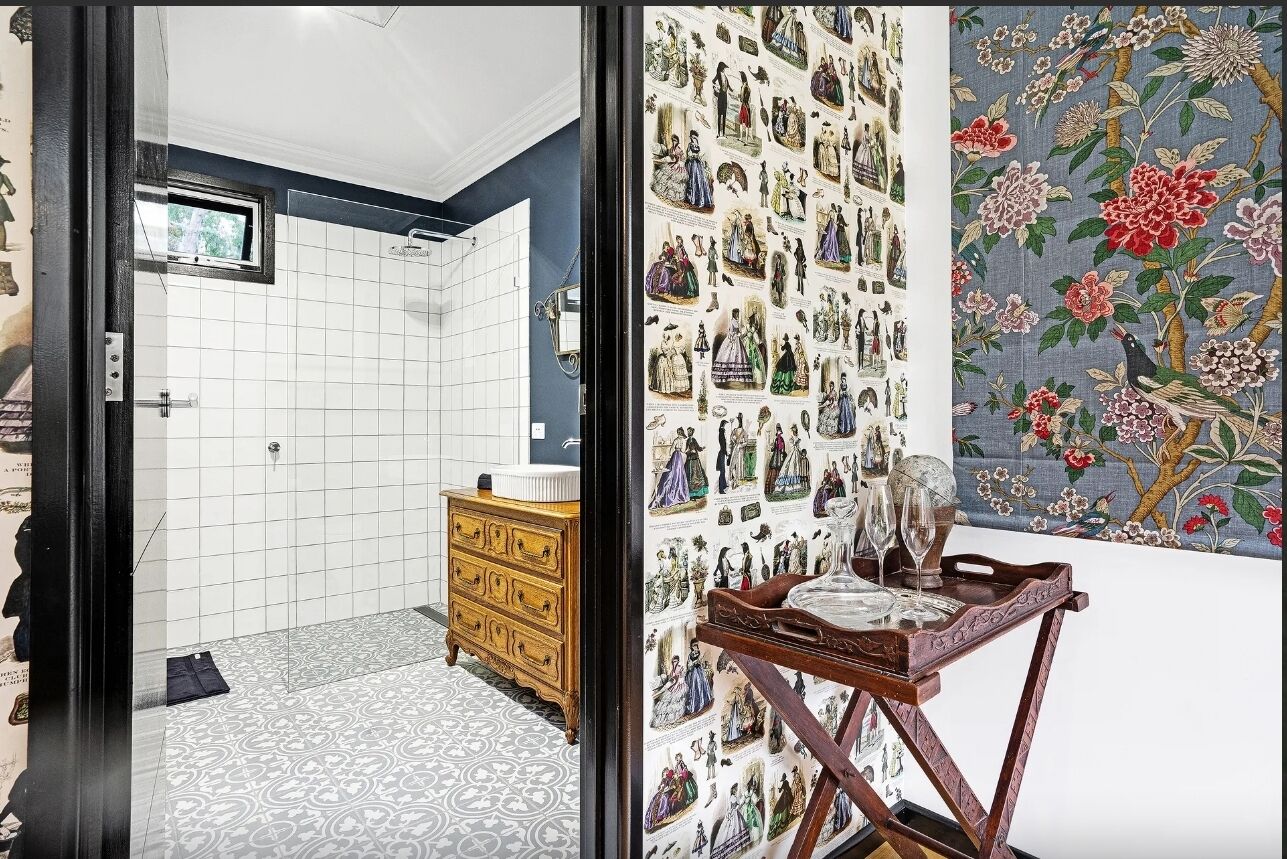 A bathroom with a tiled floor, a wooden dresser, and a wall with a floral tapestry.