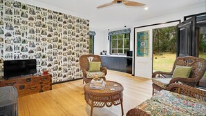 A spacious living room with a large wall of decorative prints, wicker furniture, and a ceiling fan. - Seclusion, Tram, Native Bush, Wineries, Beaches, Melbourne Icon, Village nearby (Balnarring)