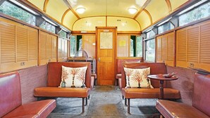 A train interior with wooden paneling, cushioned seating, and a central door. - Seclusion, Tram, Native Bush, Wineries, Beaches, Melbourne Icon, Village nearby (Balnarring)