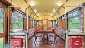 A vintage train carriage with wooden flooring, a central table, and red upholstered seats. Signs on the windows read "LOOK OUT before you step out" and "USED TICKETS PLEASE". - Seclusion, Tram, Native Bush, Wineries, Beaches, Melbourne Icon, Village nearby (Balnarring)