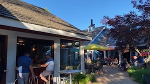 An outdoor cafe with tables and chairs, a bar area, and a covered seating area.