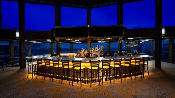 A bar area with a central island, bar stools, and a view through large windows.