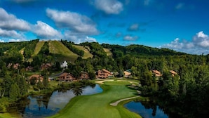 A golf course with a pond, surrounded by houses and forested hills.