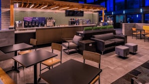 A modern indoor space with a bar area, seating arrangements, and a kitchen in the background.