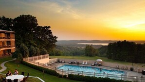 A pool area with a view of the landscape, a covered seating area, and a building with a balcony.