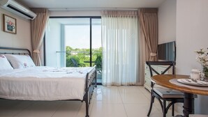 Une chambre d’hôtel comprenant un lit, une table à manger, un téléviseur et un balcon avec des rideaux.