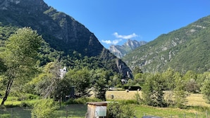 A rural landscape with a mountain, a small wooden structure, and hay bales in a field. - Pyrenees Panorama - Garonne River Apartment with Balcony (Saint-Beat-Lez)