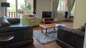 A living room with a sofa, armchair, TV stand, and a small table. - Pyrenees Panorama - Garonne River Apartment with Balcony (Saint-Beat-Lez)