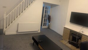 Een woonkamer met een trap, een open haard, een flatscreen-televisie aan de muur en een zwarte salontafel.