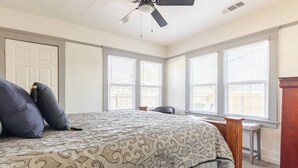 Una camera da letto con un letto, una ventola a soffitto e tre finestre con tende.