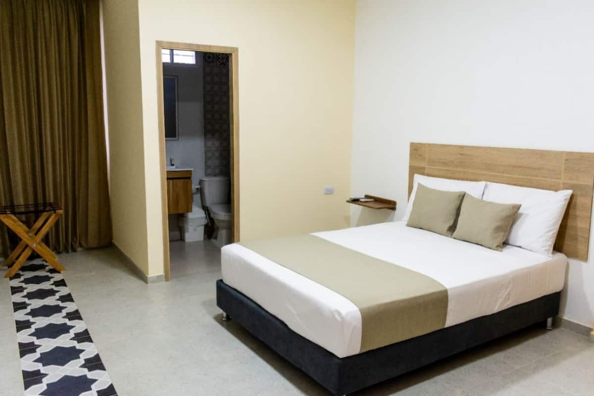 Quarto de hotel com cama, escrivaninha e banheiro visível por uma porta aberta.