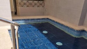 Una piscina amb un disseny de mosaic blau, una barana metàl·lica i un paviment de rajoles que condueix a la piscina.