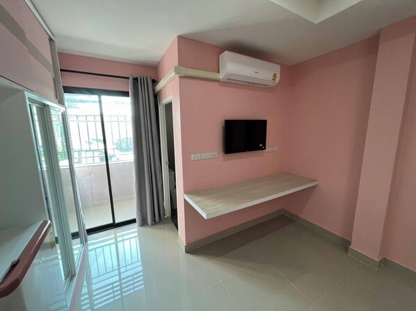 A room with a pink wall, a mounted TV, an air conditioning unit, a sliding glass door, and a wooden shelf.