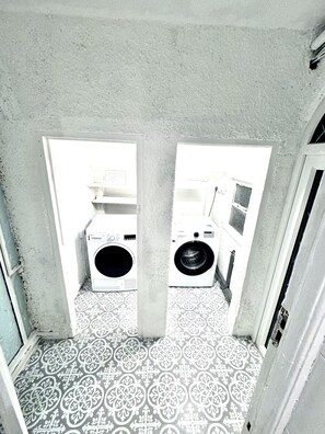 A laundry room with two washing machines, patterned floor tiles, and a concrete ceiling. - Modern Cozy 5 star 3 Bedroom House in vibrant London with wifi and free parking! (London)