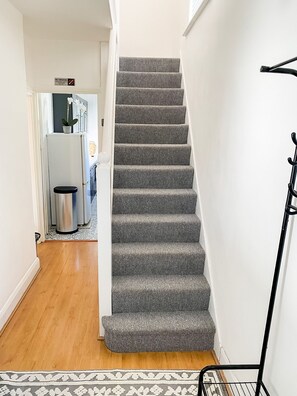 A staircase with patterned carpet, a trash can, and a metal rack on the right. - Modern Cozy 5 star 3 Bedroom House in vibrant London with wifi and free parking! (London)