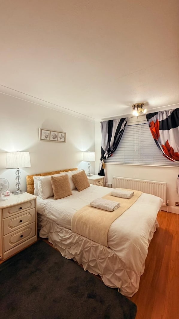 A neatly arranged bedroom with a bed, bedside tables, a lamp, and a window with curtains. - Modern Cozy 5 star 3 Bedroom House in vibrant London with wifi and free parking! (London)
