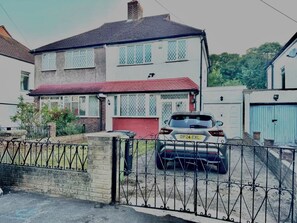 A two-story house with a red roof, a car parked in the driveway, and a gated entrance. - Modern Cozy 5 star 3 Bedroom House in vibrant London with wifi and free parking! (London)