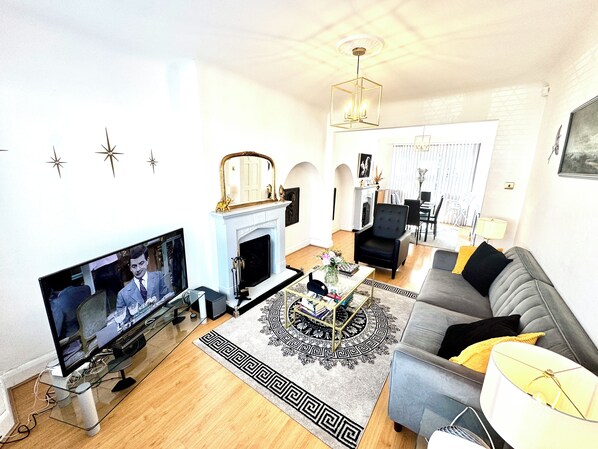 A living room with a television, fireplace, sofa, and a dining area in the background.