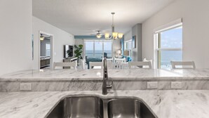 Cocina moderna con encimera de mármol, pileta de acero inoxidable y vista a un área de comedor con un ventanal frente al océano.