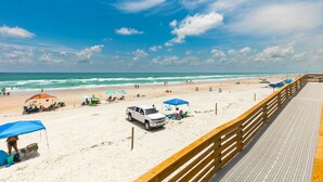Una playa con un paseo marítimo de madera, sombrillas, sillas de playa y un camión blanco.