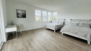 Ein Schlafzimmer mit zwei Betten, einem Schreibtisch und großen Fenstern.